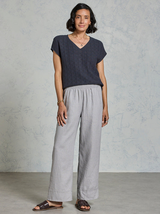 Woman wearing a dark top and light gray pants against a plain background