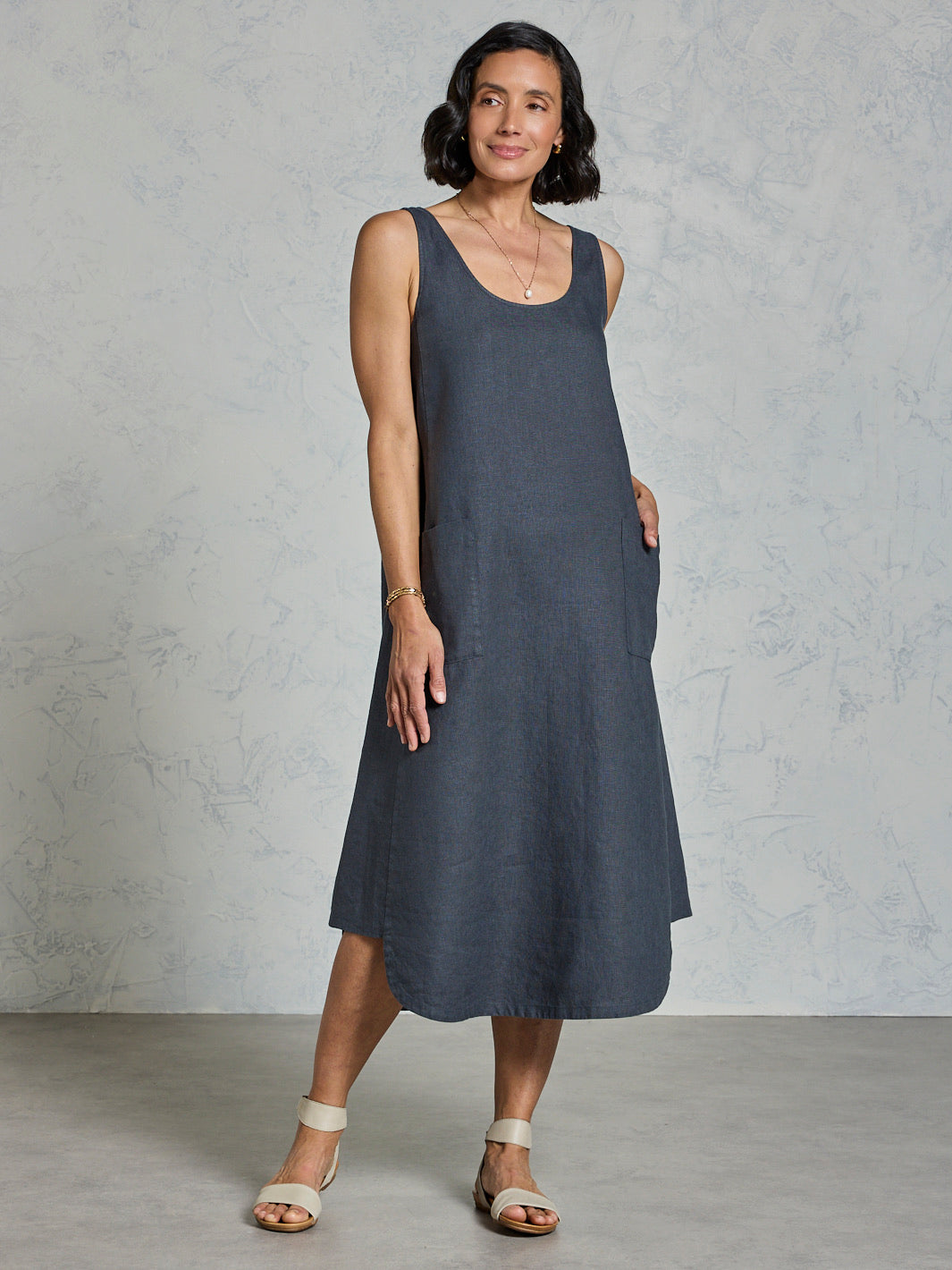 Woman wearing a dark sleeveless dress against a plain background