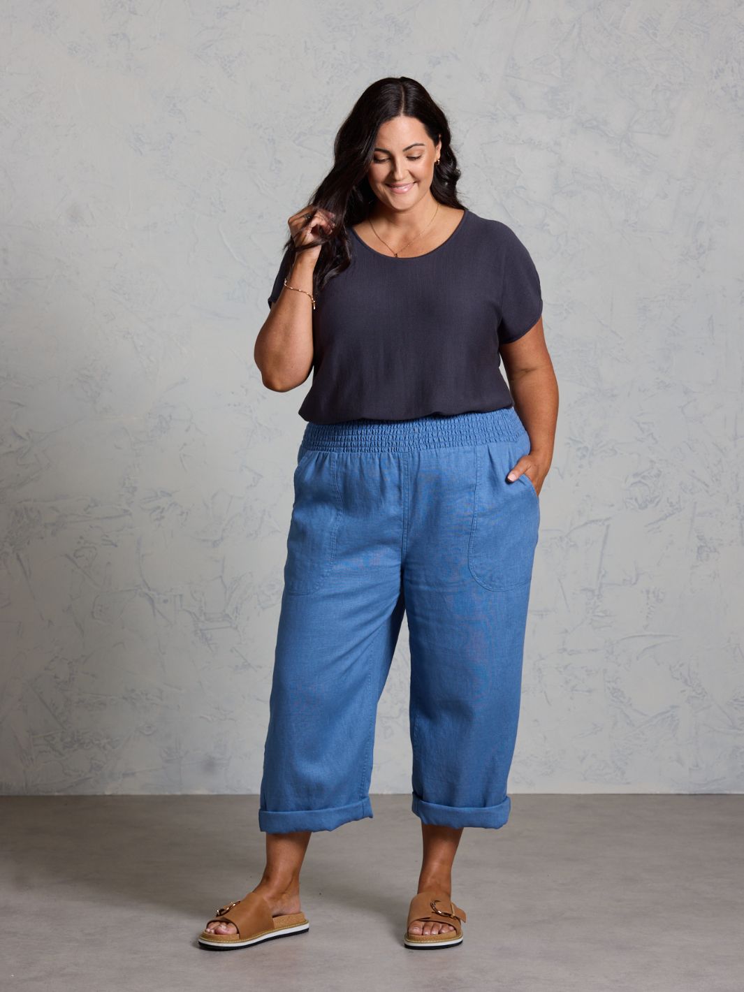Woman wearing a black top and blue pants against a gray background