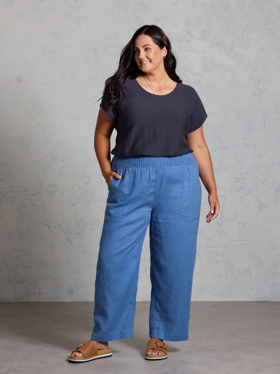 Woman wearing a navy t-shirt and blue pants against a gray background
