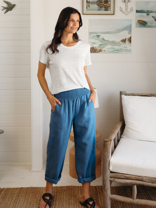 Woman wearing a white t-shirt and blue pants standing in a room with a chair and decorative items on the wall.