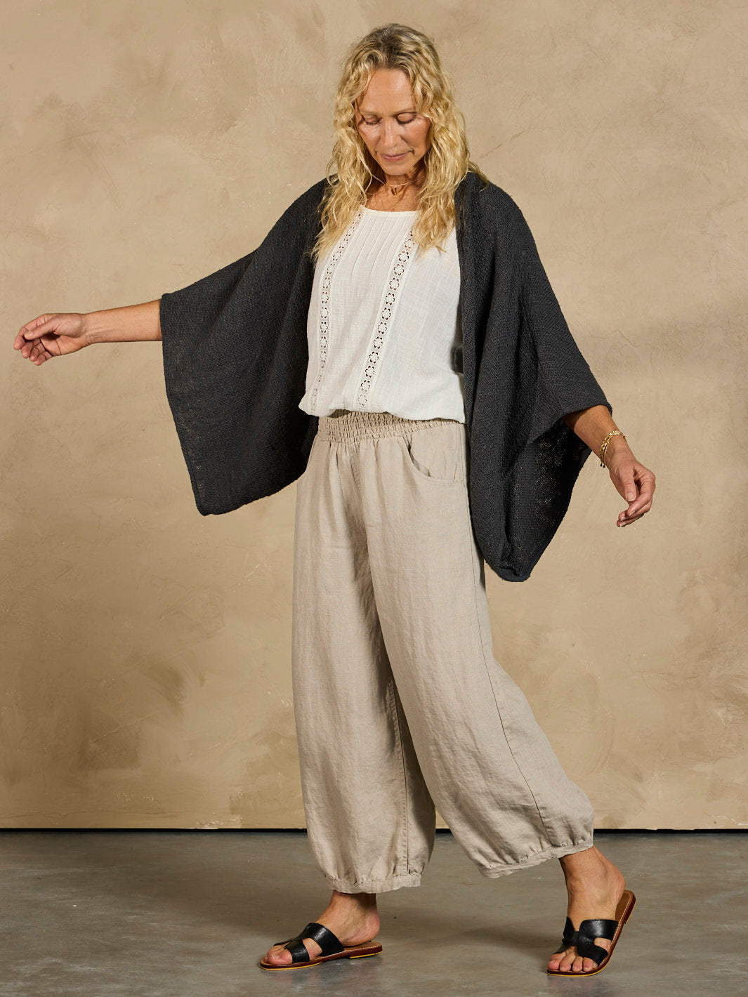 Woman wearing a black cardigan and beige wide-leg pants against a beige background