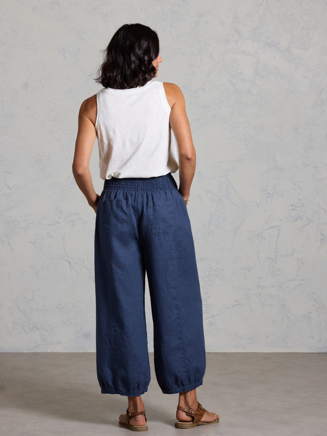 Woman wearing a white sleeveless top and blue wide-leg pants against a gray background