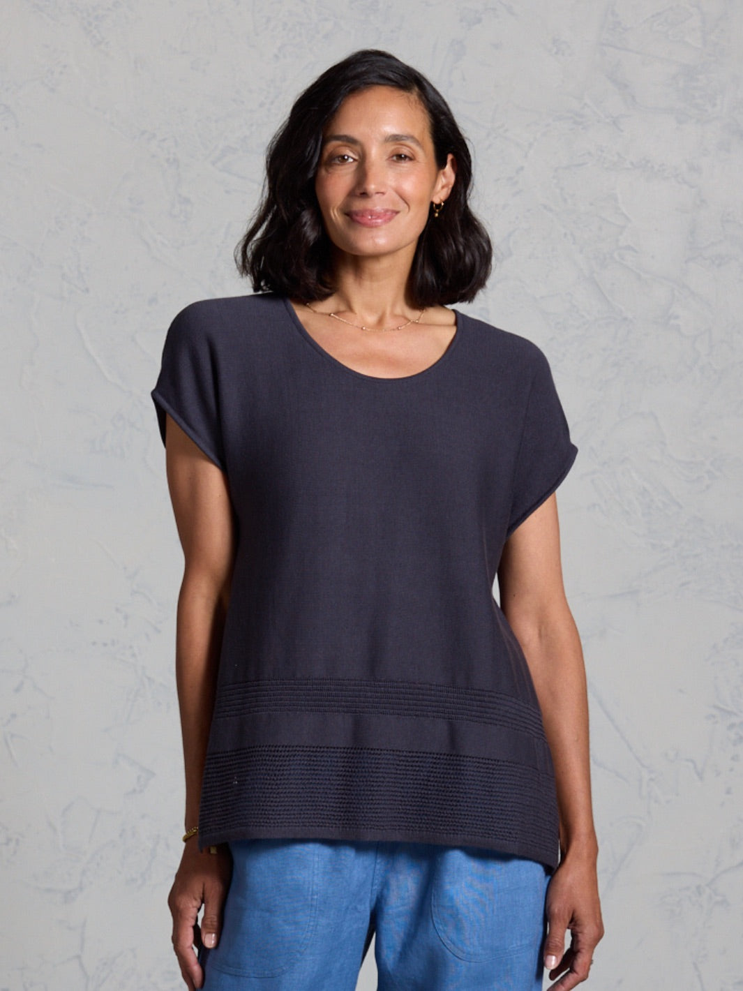 Woman wearing a dark blue top and blue pants against a gray background