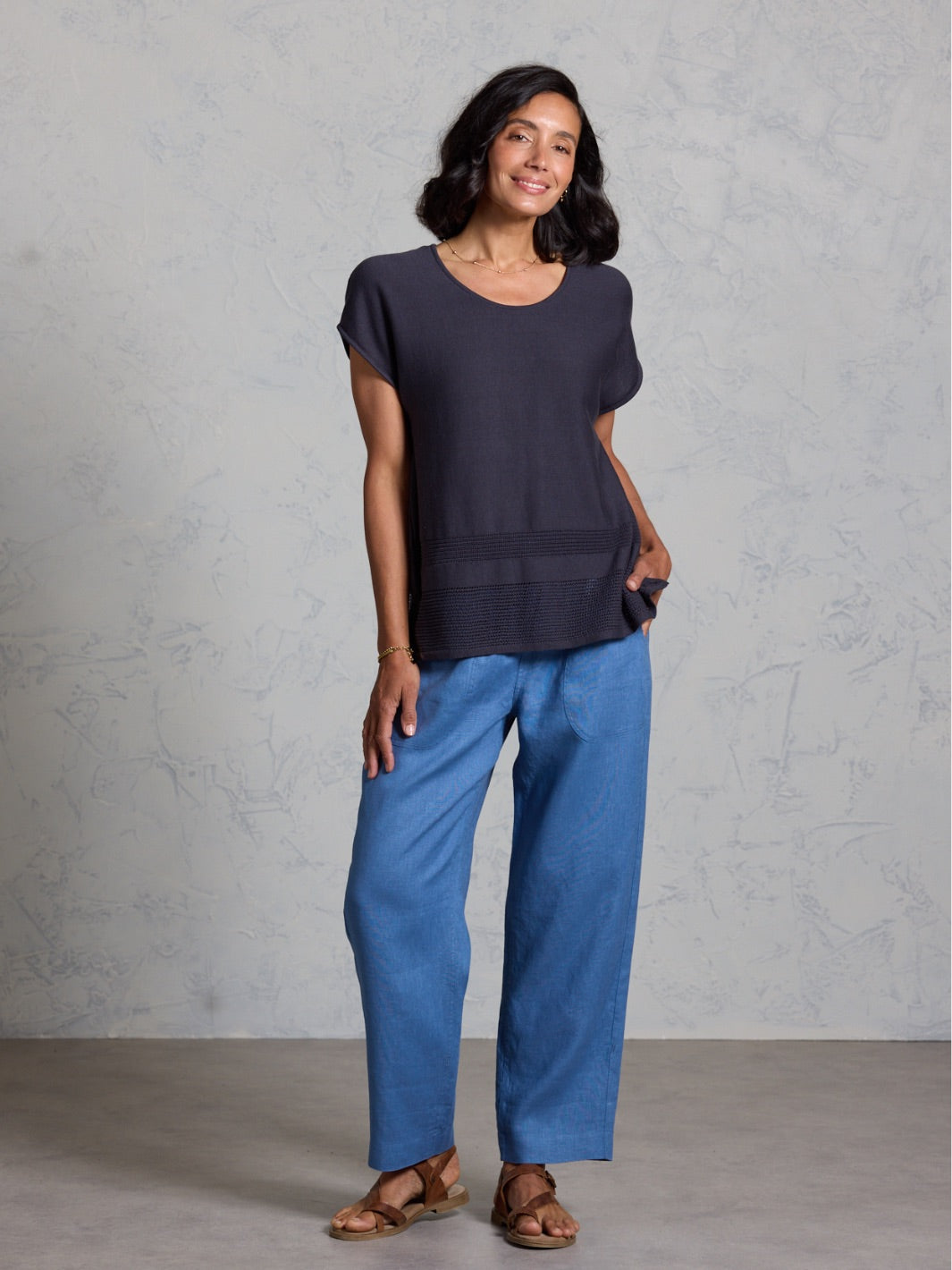 Woman wearing a black top and blue pants against a gray background