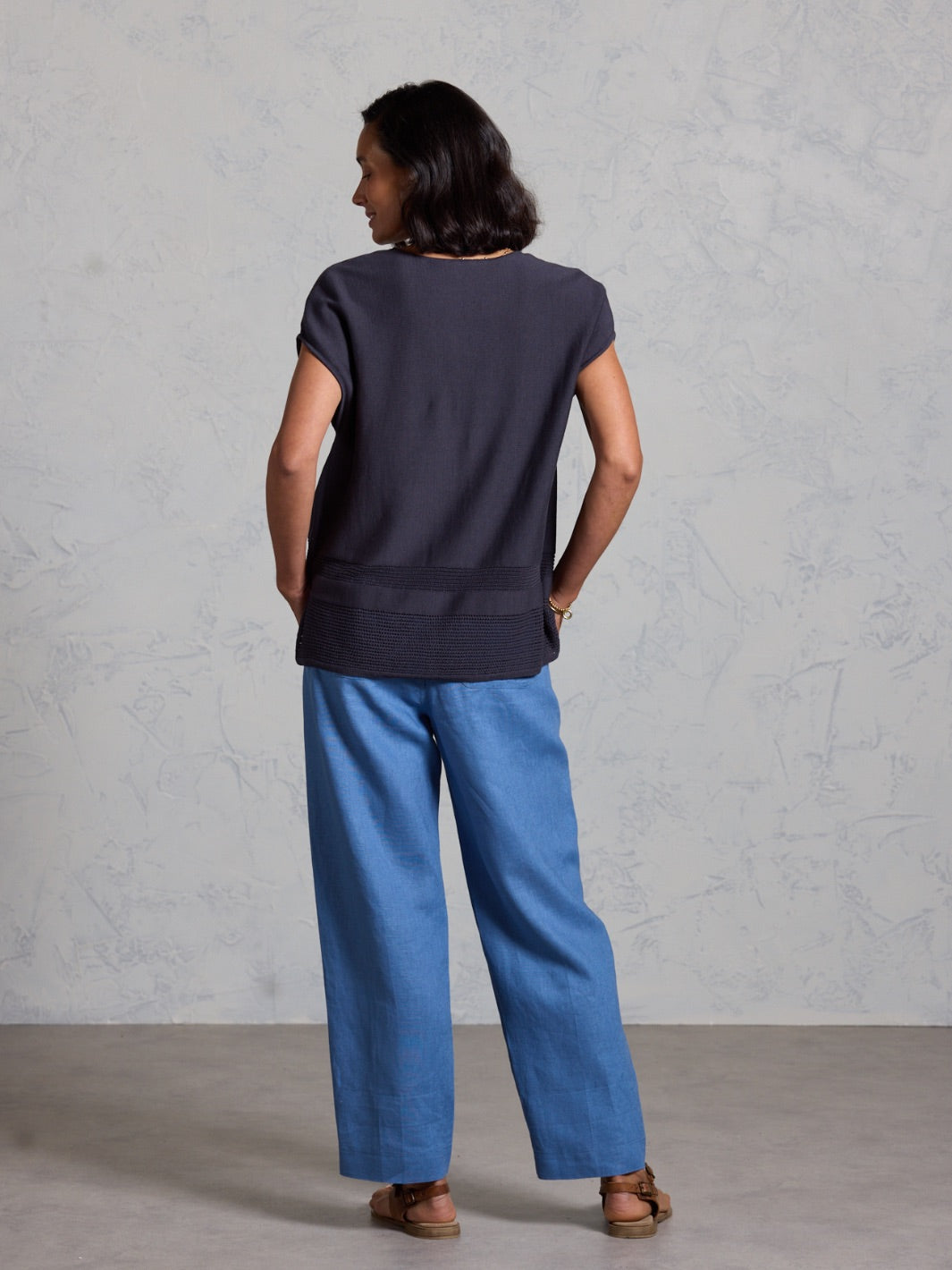 Person wearing a dark top and blue pants against a gray background