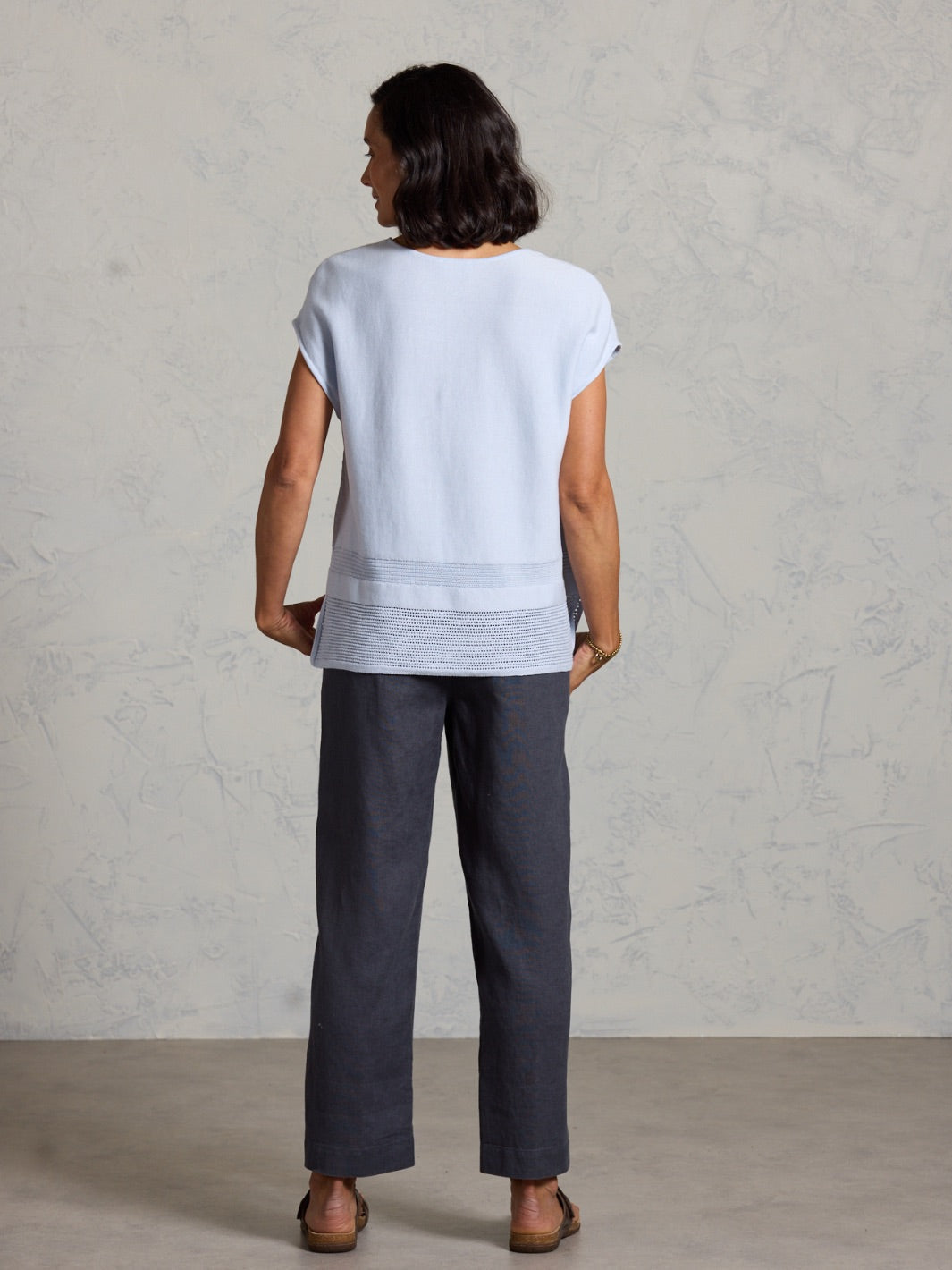 Woman wearing a light blue top and dark pants against a plain background