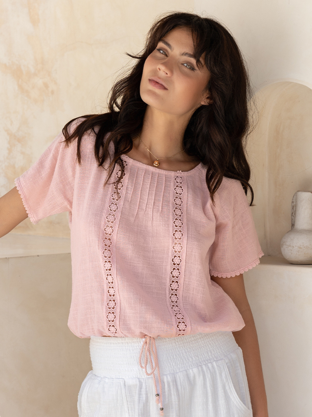 Woman wearing a pink blouse with lace details against a neutral background