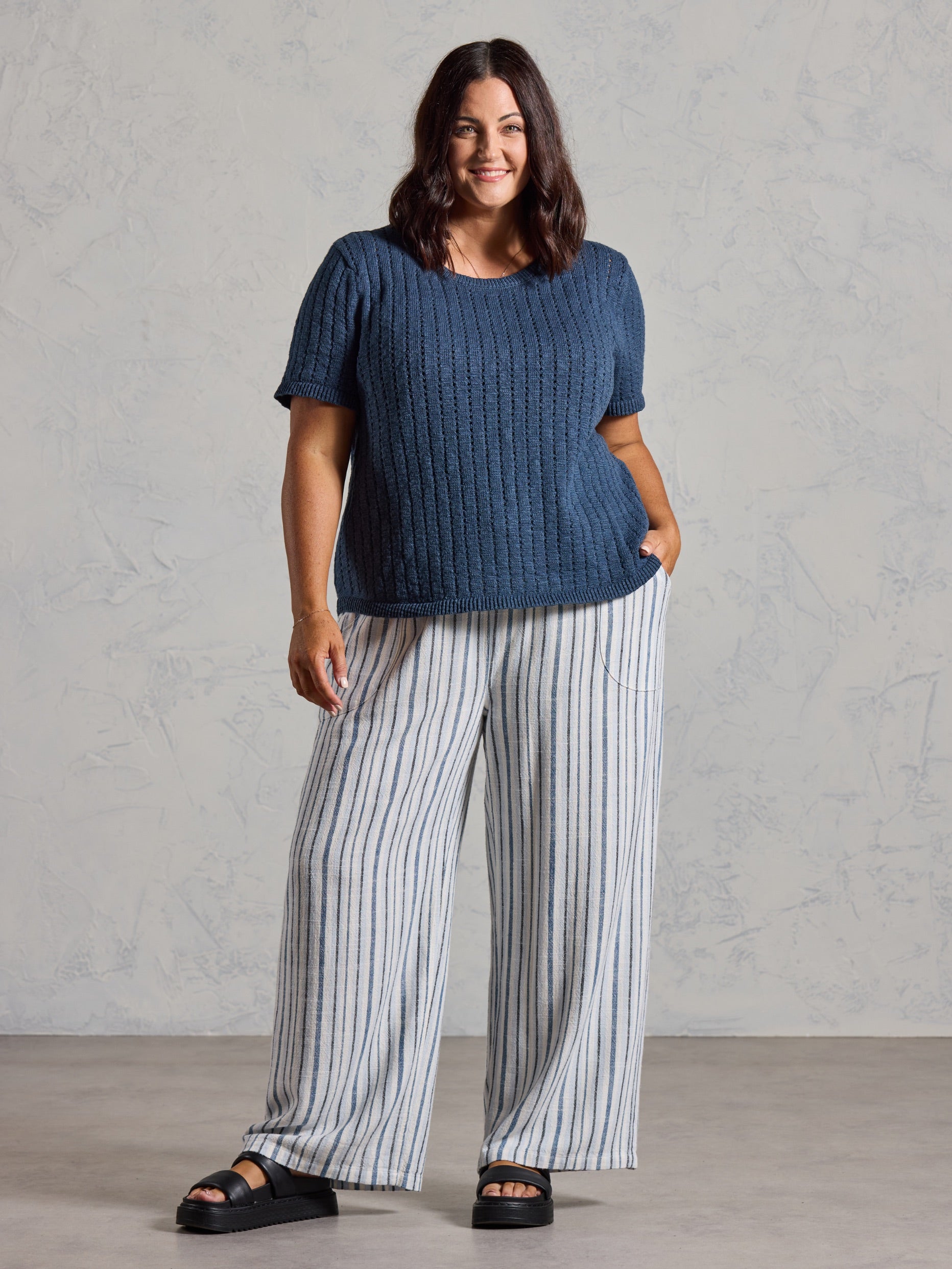 Curve model in the Agni Cotton Linen Knit Top in navy, styled with wide leg striped linen pants.