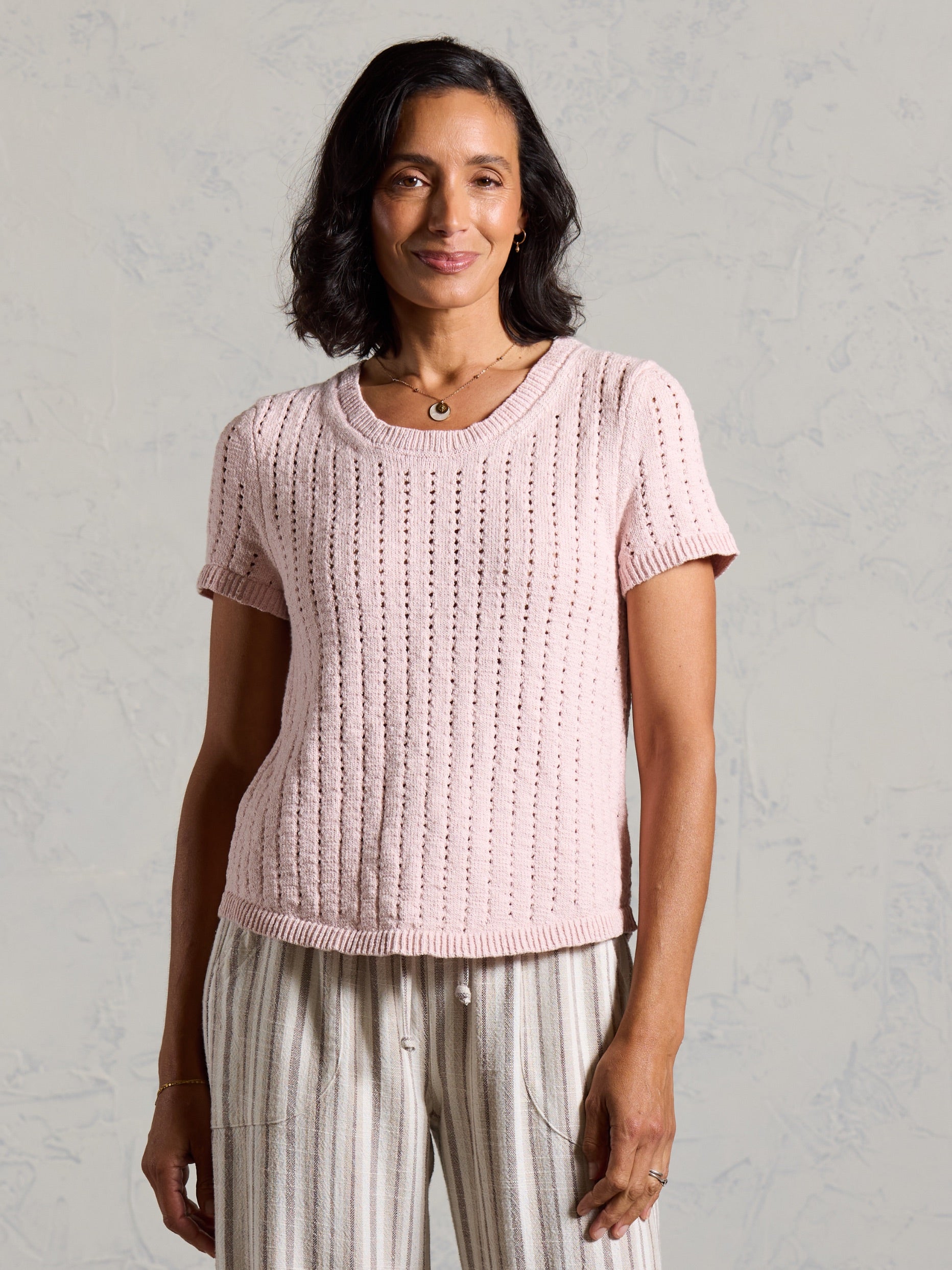 Front view of the Agni Cotton Linen Knit Top in rosewater, worn with striped linen pants.
