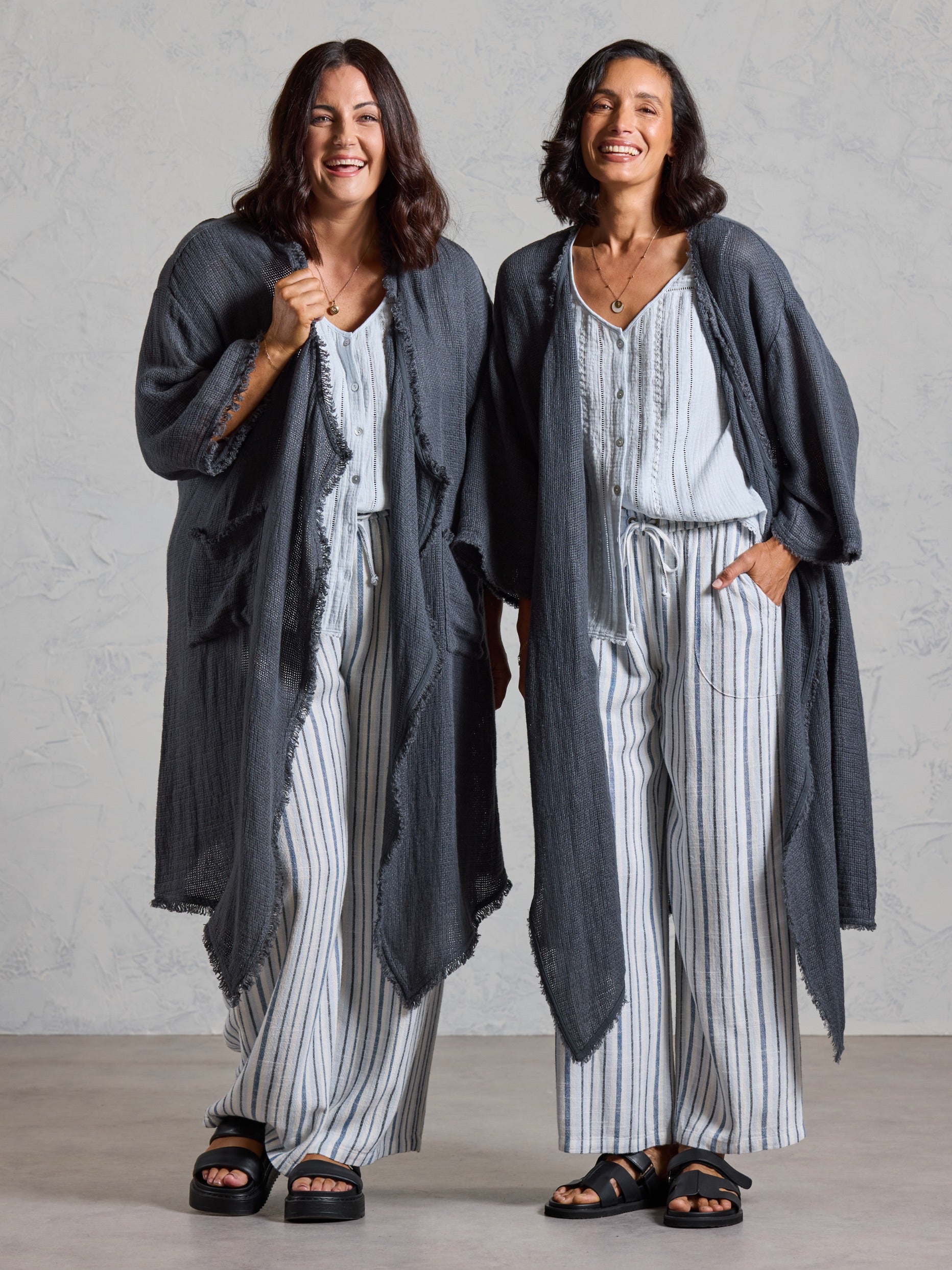Two models wearing the Laguna French Linen Kimono in charcoal with white tops and striped linen pants