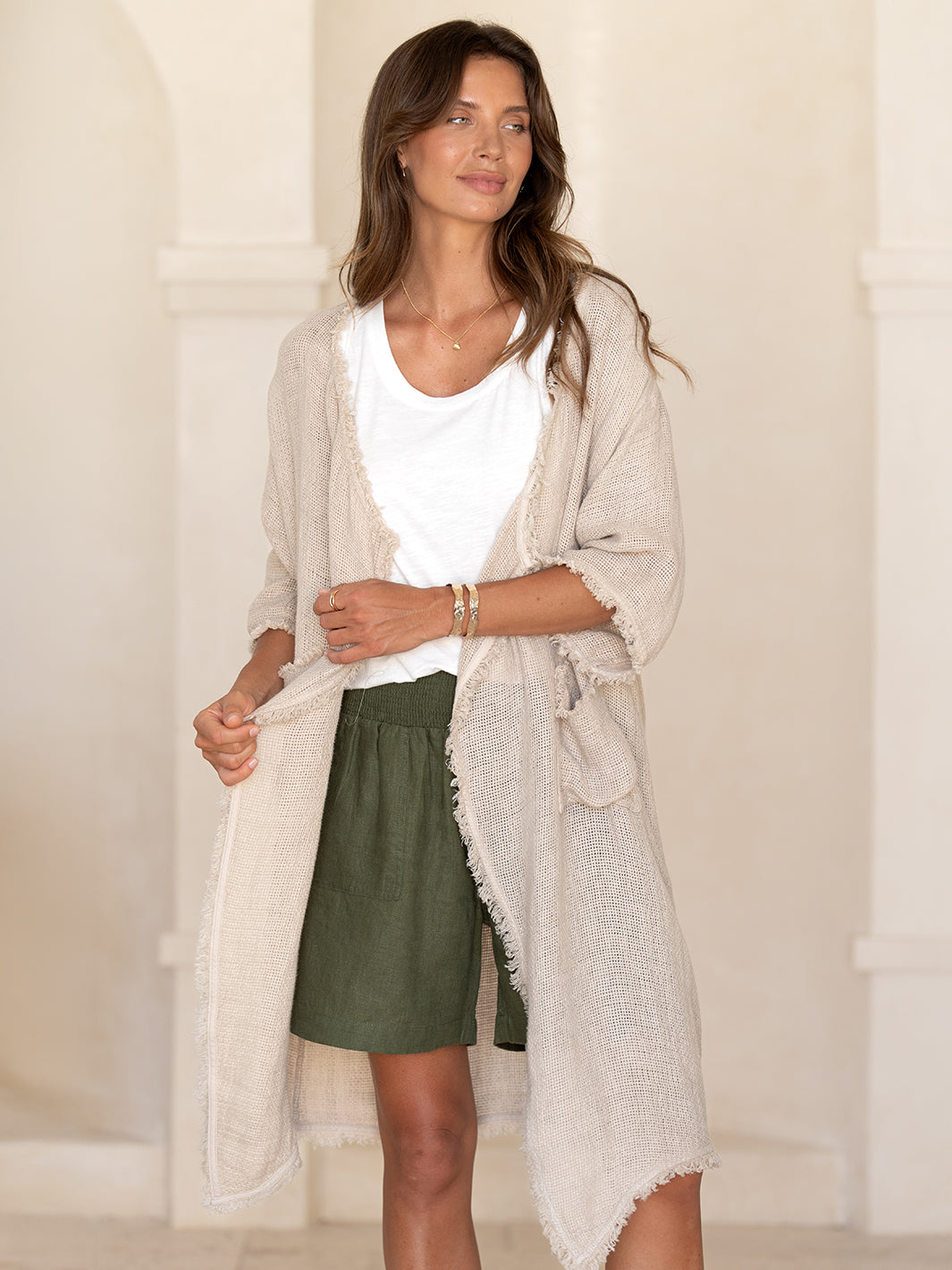 Model wearing the Laguna French Linen Kimono in natural over a white tee and olive linen short, showing the fringed front edge.