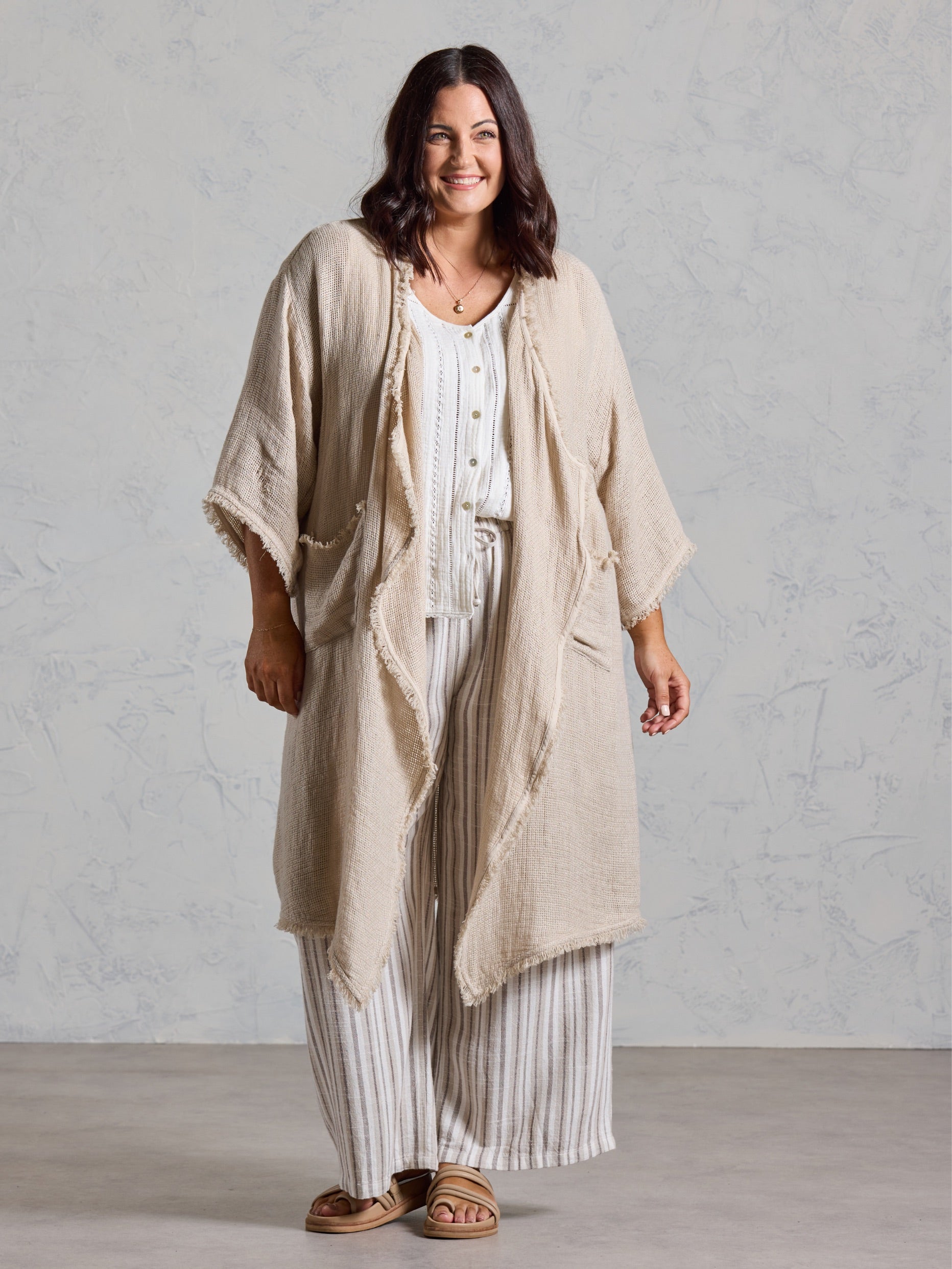 Curve model in the Laguna French Linen Kimono in natural, layered over a white top and striped linen pants.